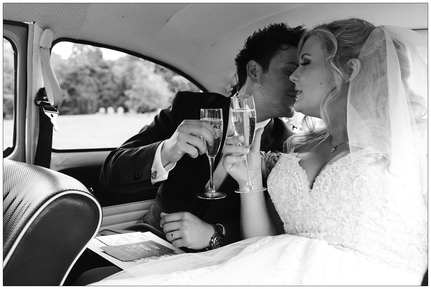 Bride and groom inside the car after the wedding with glasses of fizz.
