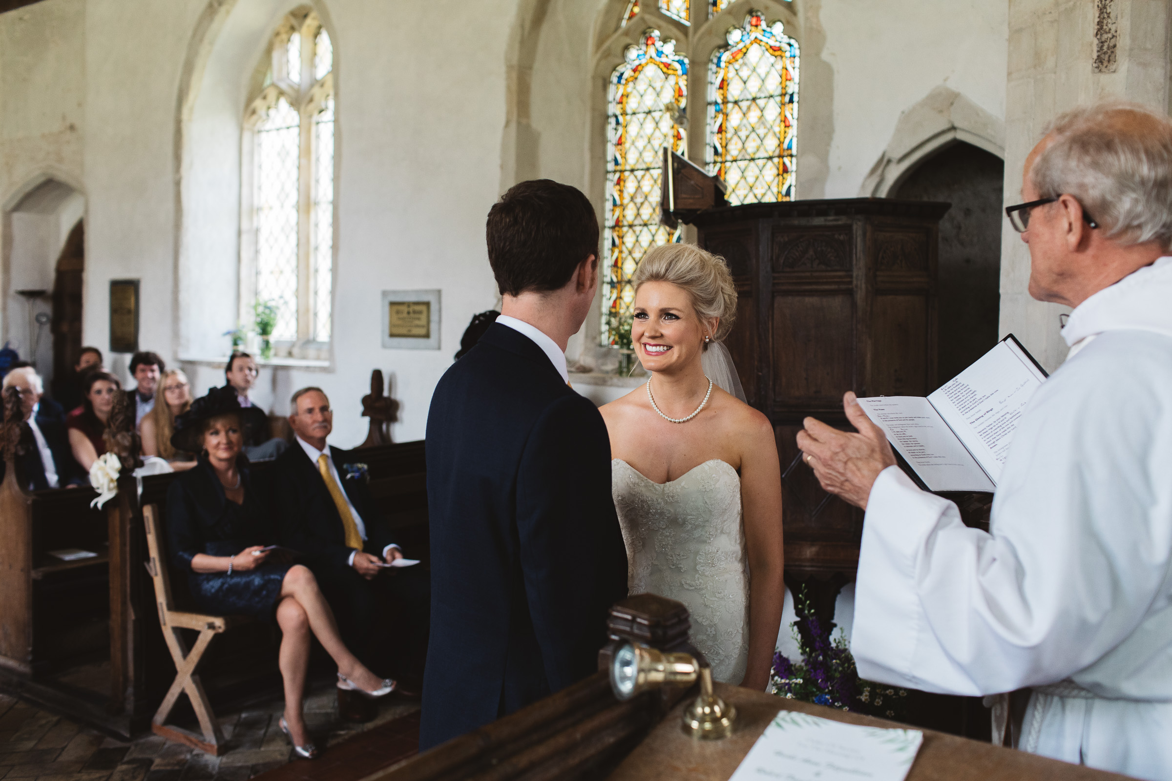 Bride smiling at groom during wedding ceremony at St Peter & St Paul's Church in Alpheton