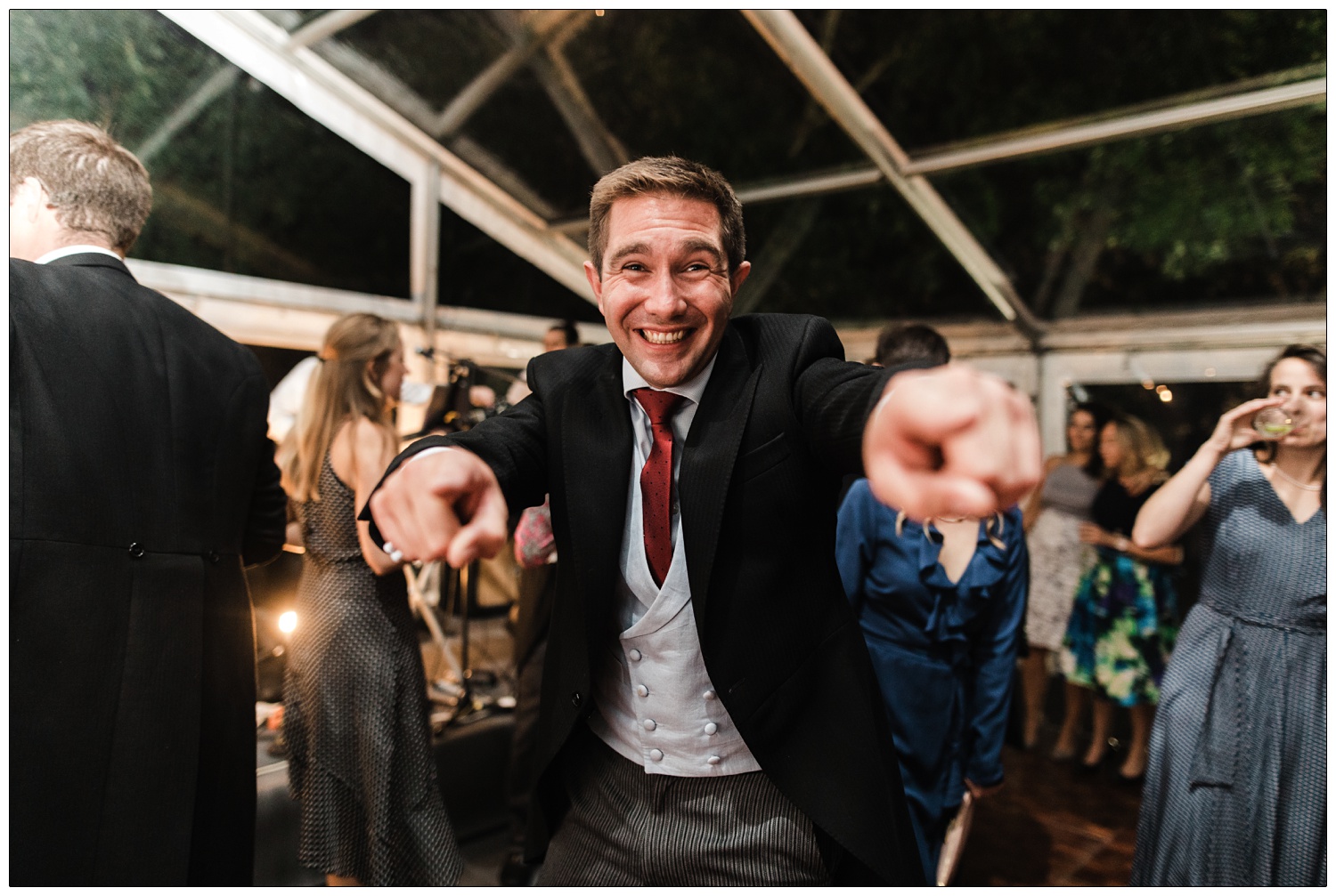Man at a wedding reception is smiling on the dancefloor and pointing at the camera. At a wedding near South Woodham.