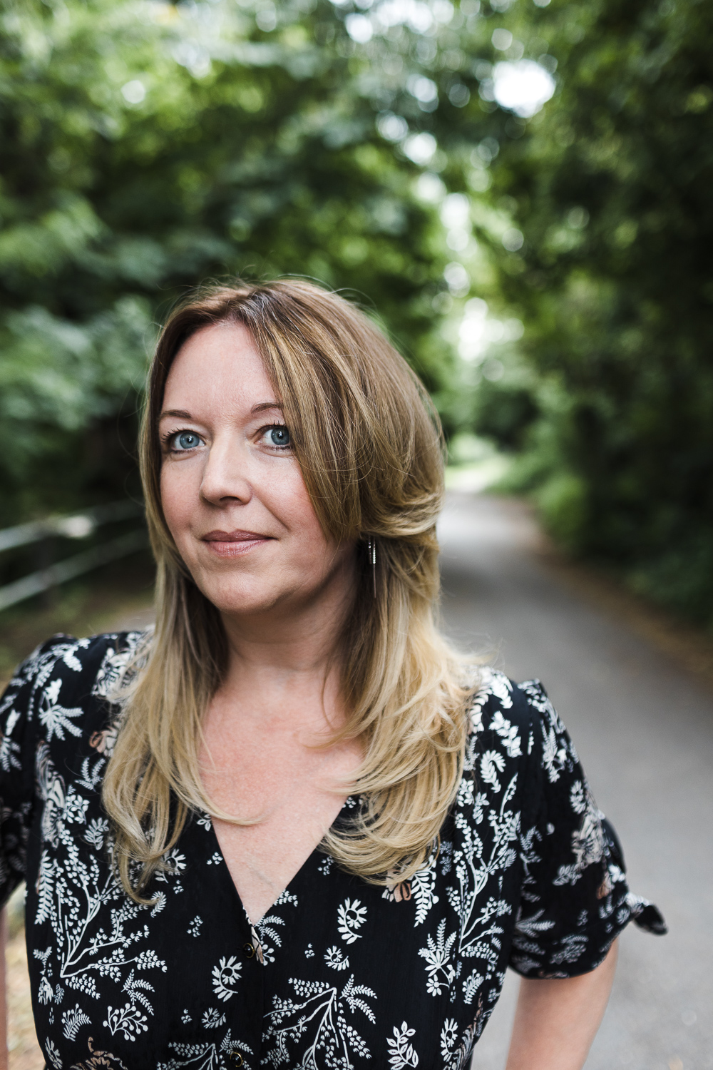 Tracy the photographer from Tracy Morter Photography. Wearing a black and white Temperley dress. Standing outside in a tree lined road in South Woodham.
