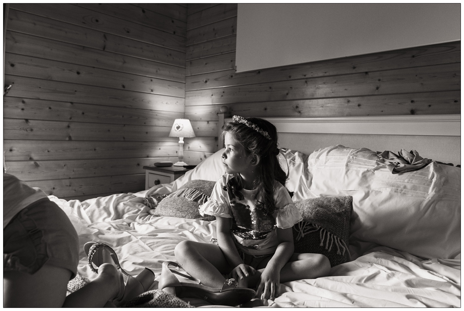 A young girl sits on a bed on the morning of a wedding.