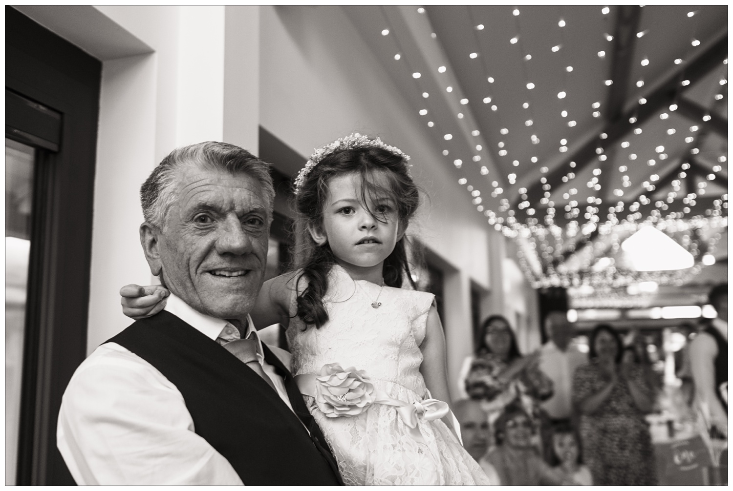A man with his young granddaughter. She is wearing a flower girl dress.