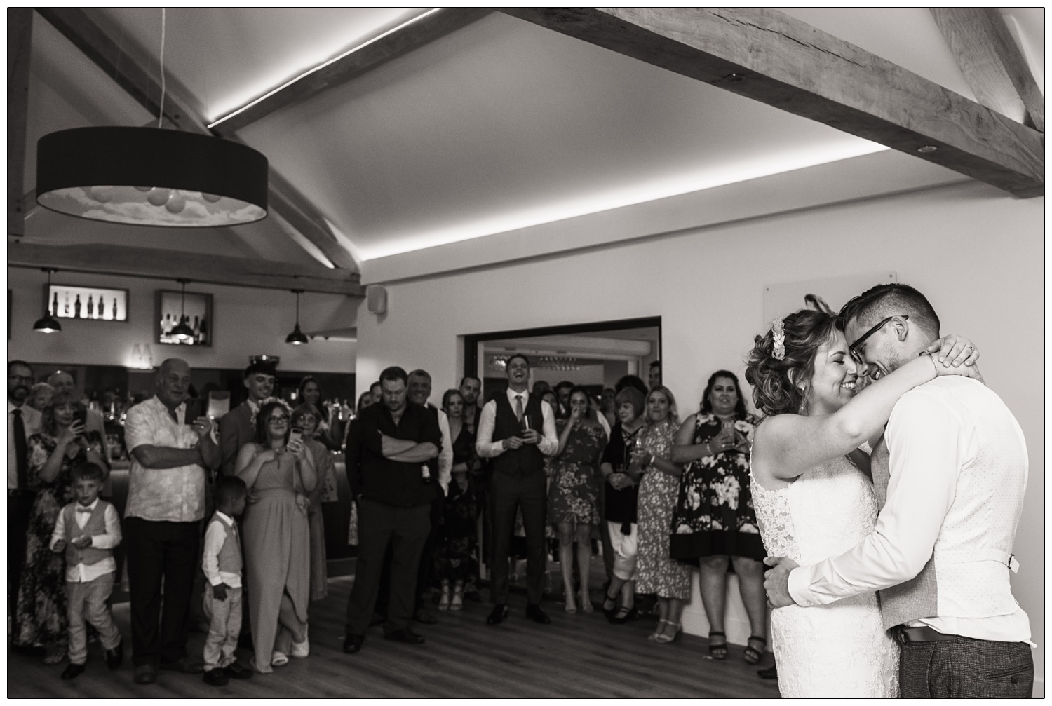 A black and white photograph of a newly married couple having their first dance. The guests are watching. At Fynn Valley Terrace wedding venue.