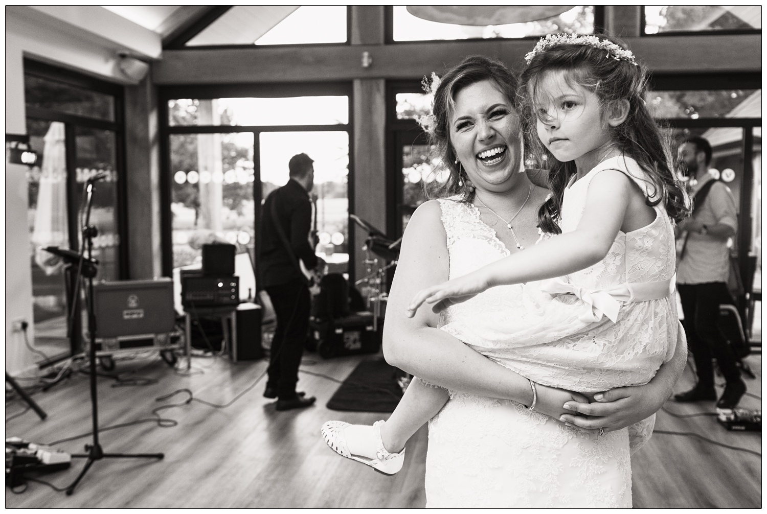 A woman on her wedding day is holding her daughter and laughing as the band play behind.
