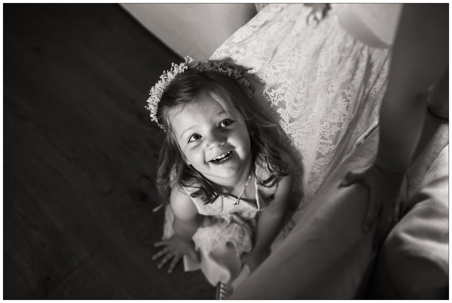 A small flower girl sitting on the floor and smiles whilst looking up.