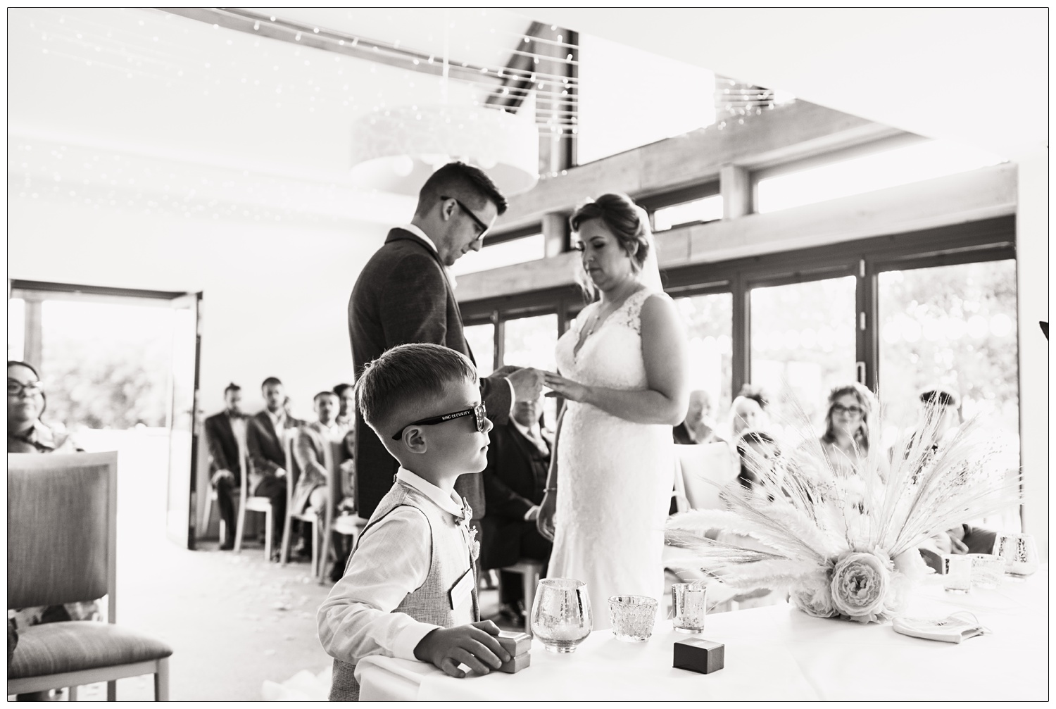 Boy looking after the ring boxes during a wedding ceremony. He has sunglasses on, the words ring security are written on the arm of the glasses.