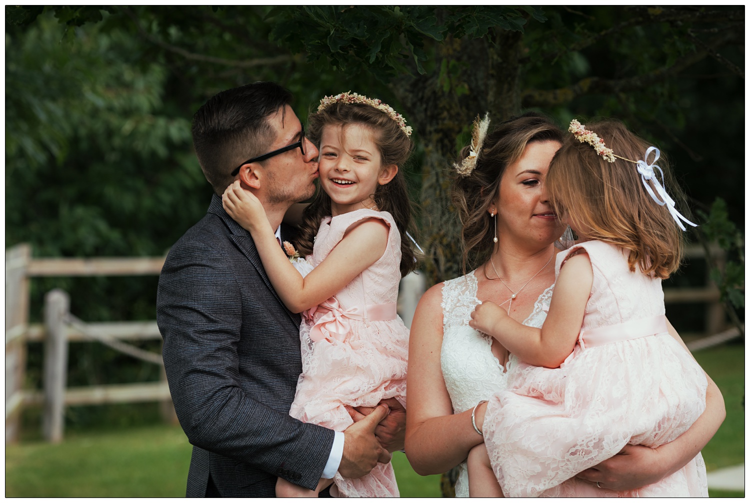 A man kisses his young daughter on the cheek while she smiles, his new wife holds their other child. At their Fynn Valley Terrace wedding.