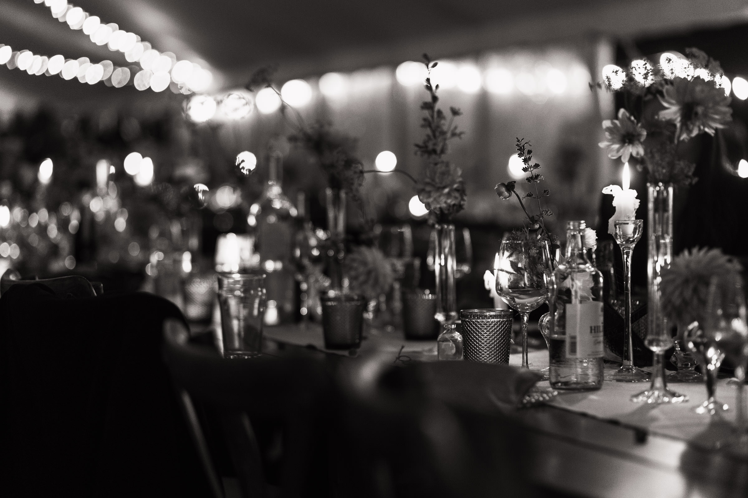 A long wedding breakfast table late at night in a marquee. A wedding near South Woodham Ferrers. There are candles and empty glasses, fairy lights on the ceiling. Marquee from Sail & Peg.