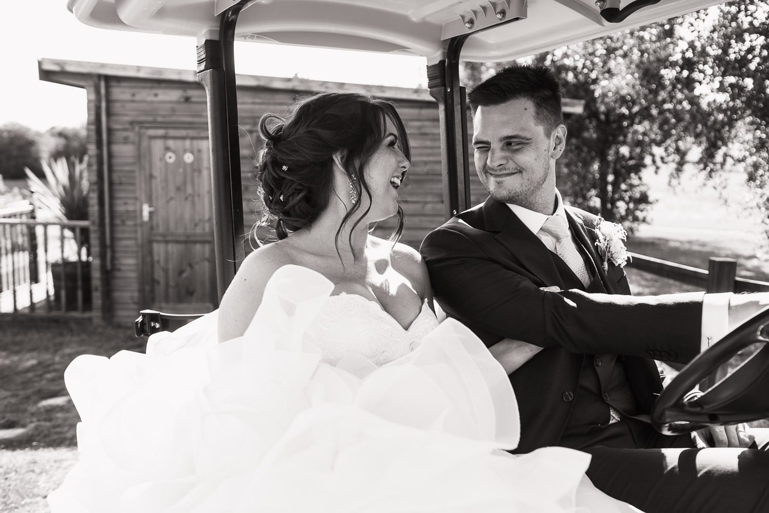 A bride and groom in a golf cart at a wedding in Essex. The bride is laughing and groom is winking.