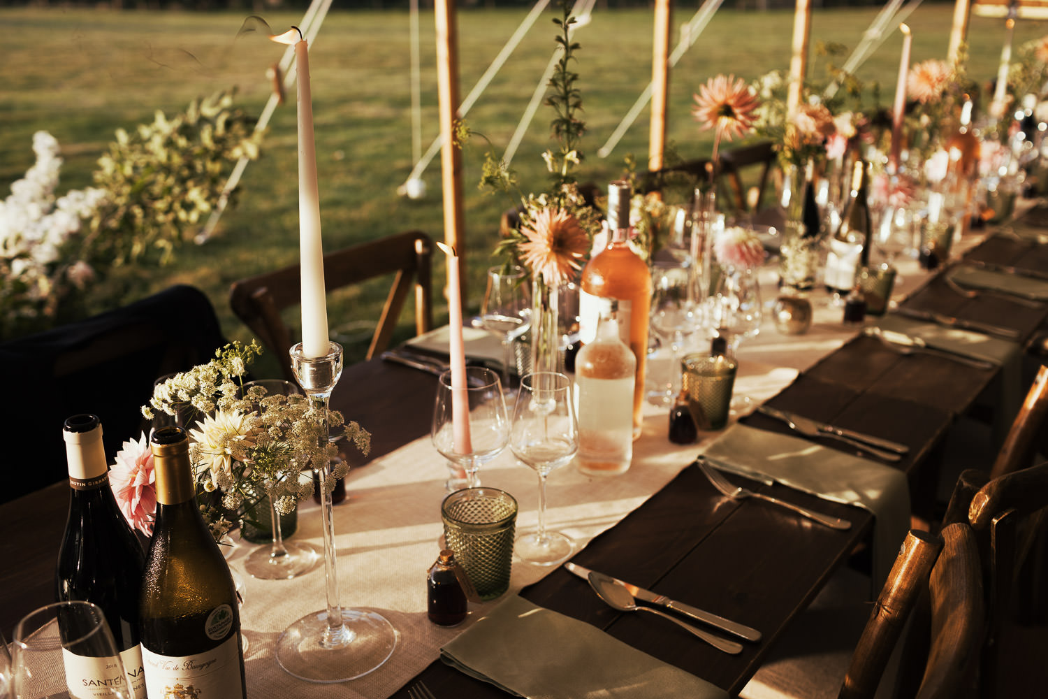 A long wooden table set with flowers, candles and wine for a wedding.

Hosted in a Sail & Peg marquee in the garden of Wellinditch Farmhouse. This home-hosted wedding near South Woodham Ferrers was by local documentary photographer Tracy.