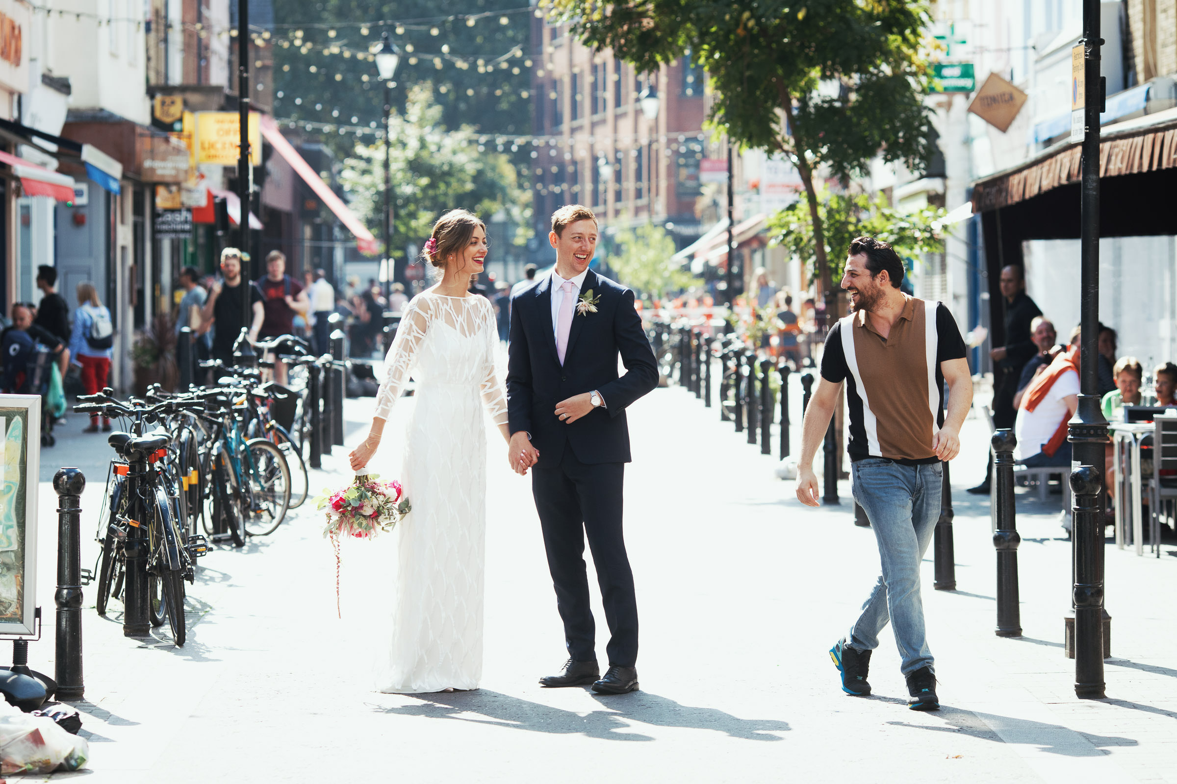 Natural London wedding photography. Bride and groom in Exmouth Market after their wedding at Union Chapel. A stranger congratulates them. The bride is wearing Halfpenny. By documentary wedding photographer Tracy.