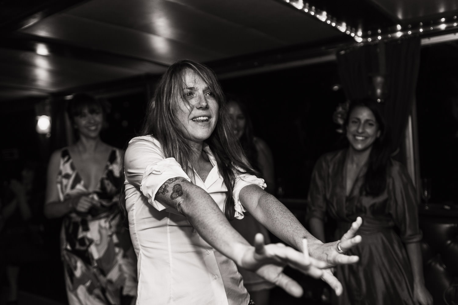 Black and white candid photograph of a woman dancing at a wedding, she's holding a cigarette.