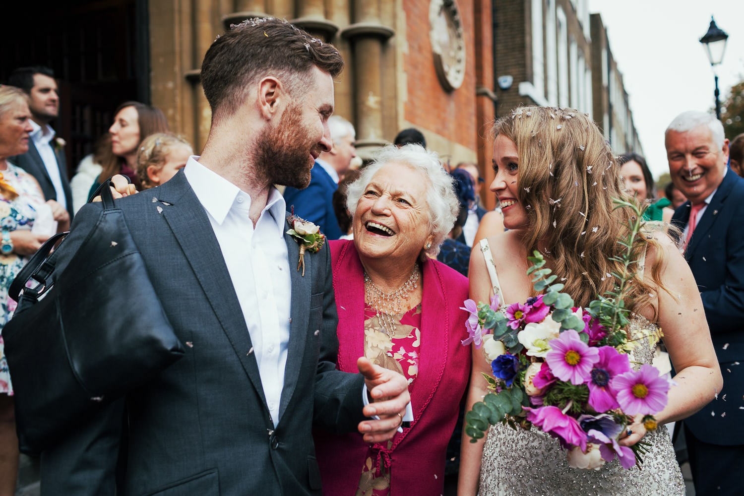 London wedding photography outside the Union Chapel. A grandmother looks up at the groom, the bride is next to her holding flowers.