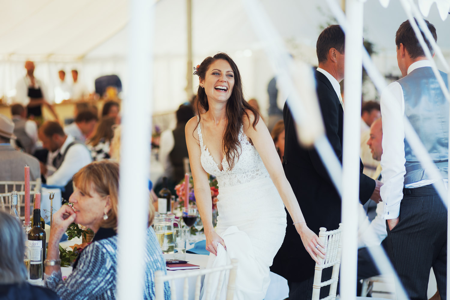 An Essex bride is smiling as she stands up from her wedding breakfast table in a marquee. A Latchingdon wedding by the River Crouch. Bride is wearing Stella York 6648 from The Wedding Shop in Colchester.