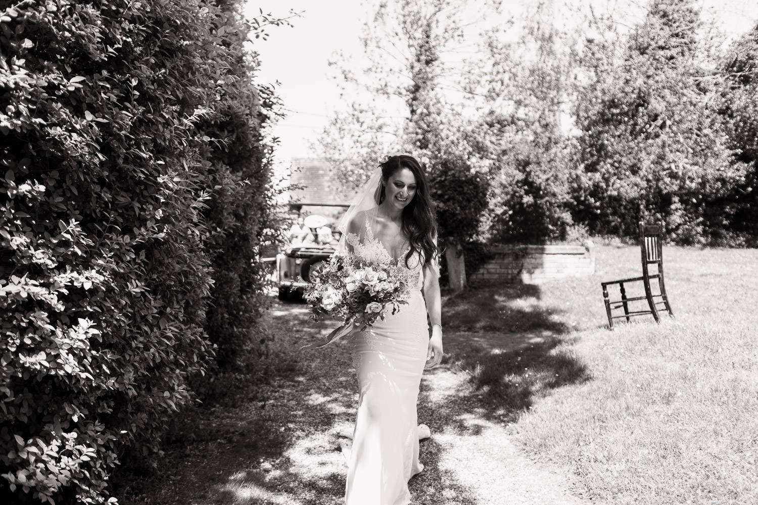 A smiling bride with long dark hair walks down the gravel path to the All Saints church in Purleigh Essex.