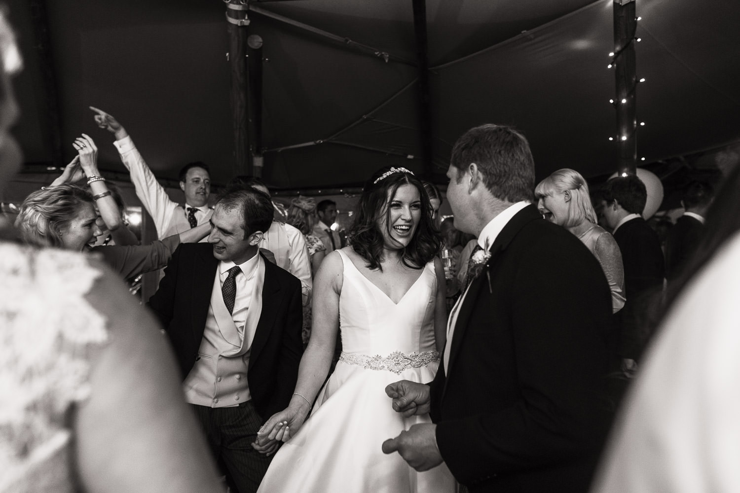 Bride and groom are dancing together in the middle of a packed dance floor.