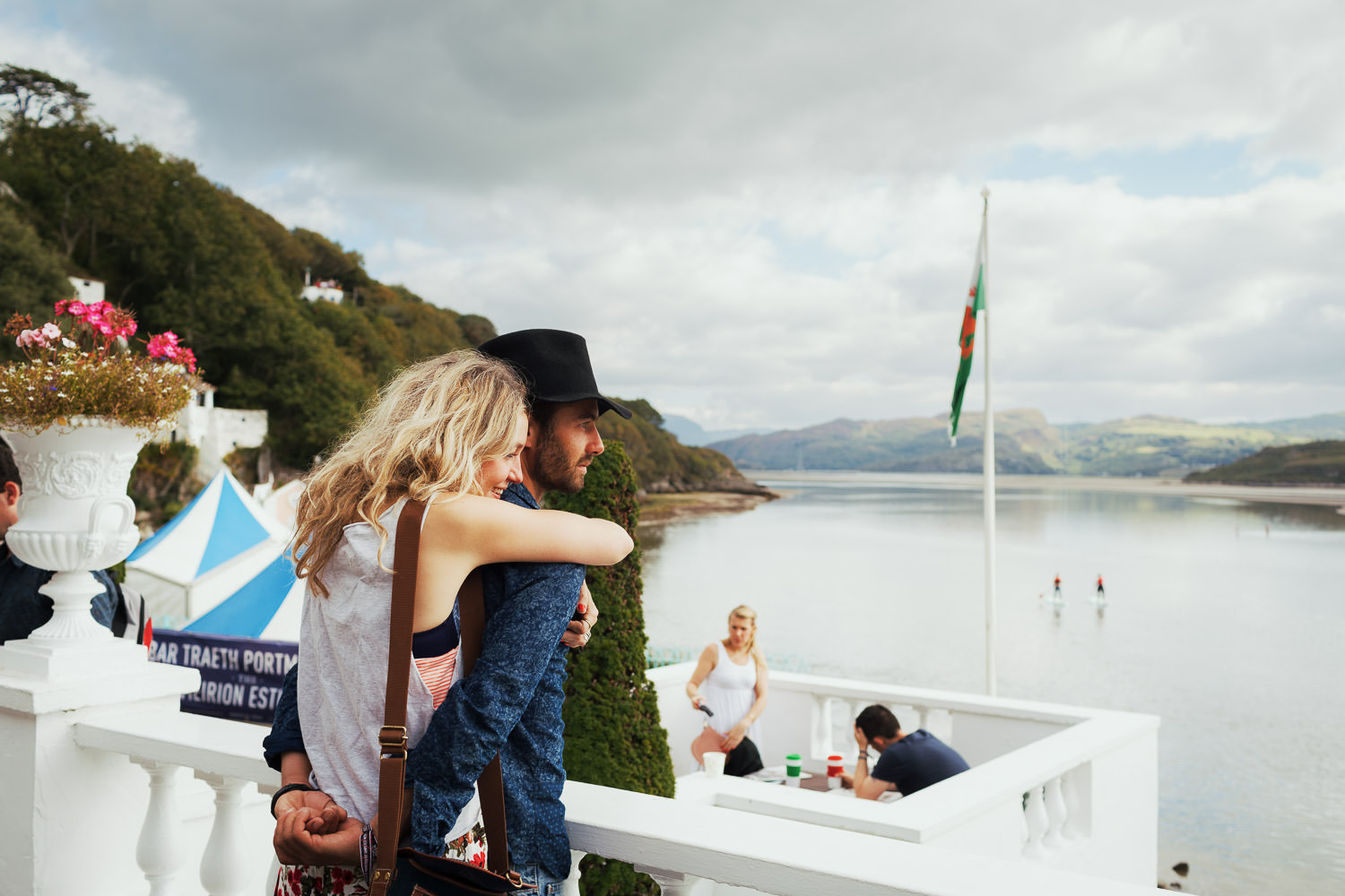 A woman hugging a man from behind. They are at Festival Number 6. They are overlooking the Dwyryd Estuary at Portmeirion Village.