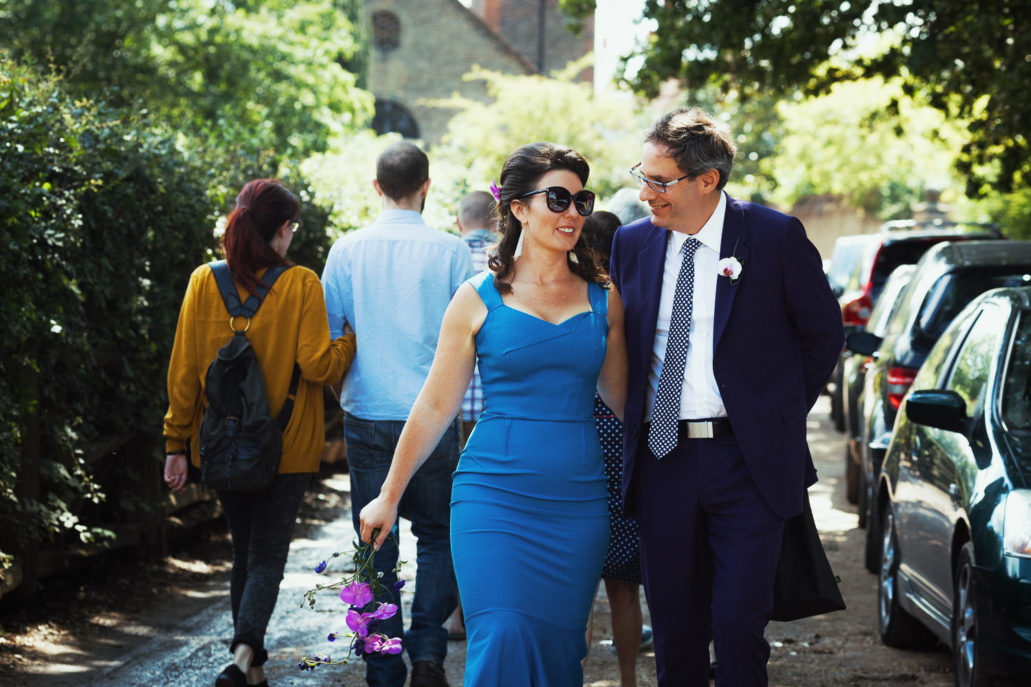 A couple on their wedding day walk to Petersham Nurseries for a wedding meal. The bride is wearing blue and the groom is in purple.