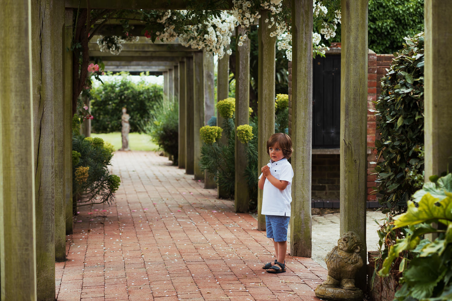 A little boy standing under a pergola.