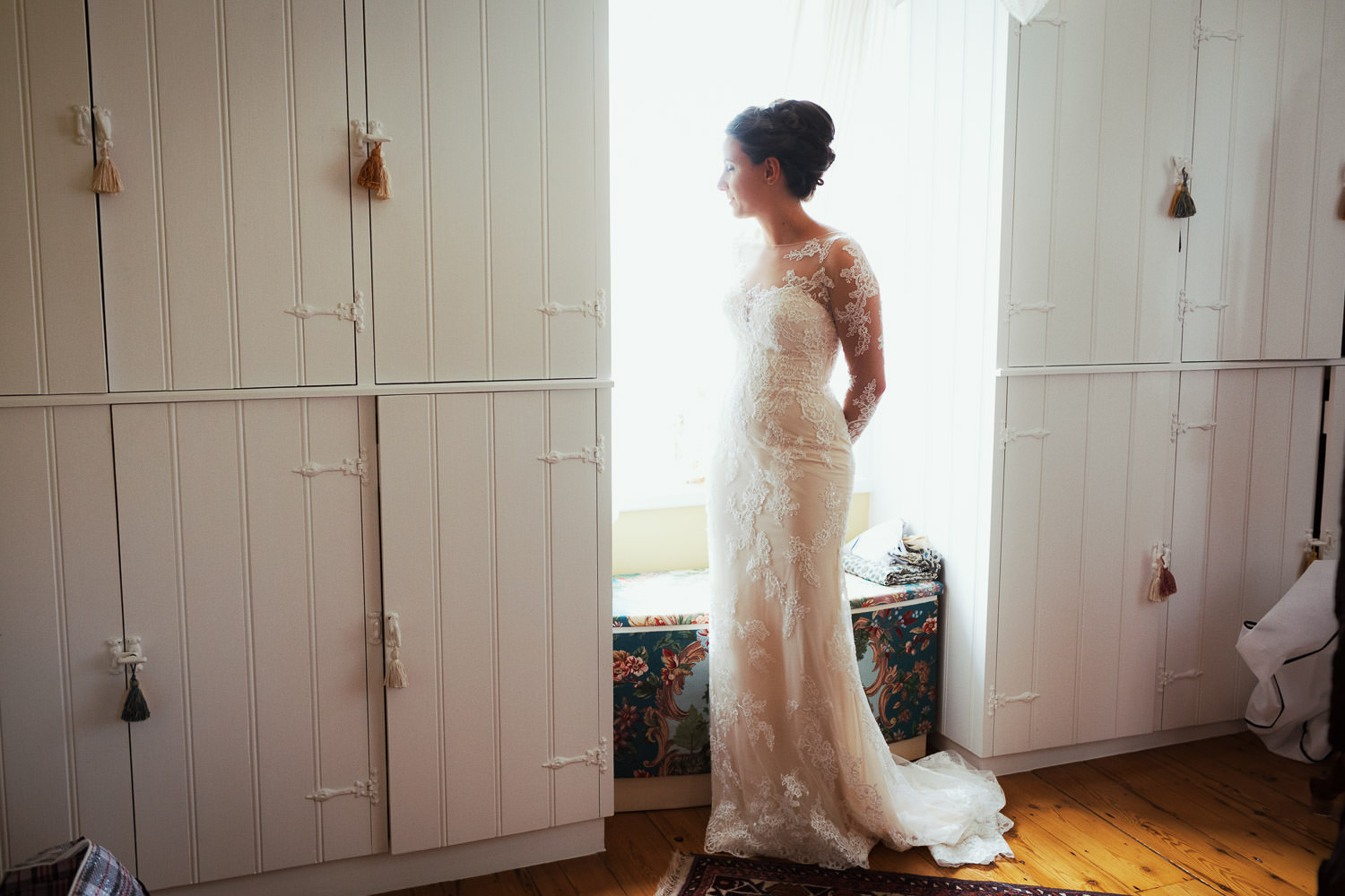 Bride in a bedroom with her lace dress on.