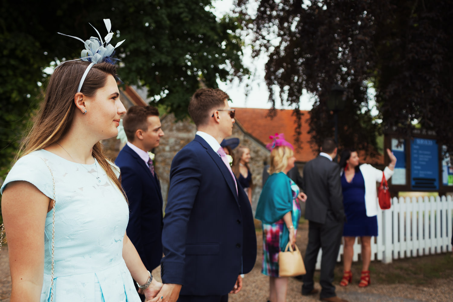 A couple holding hand outside a church. The woman is wearing a blue dress and fascinator.