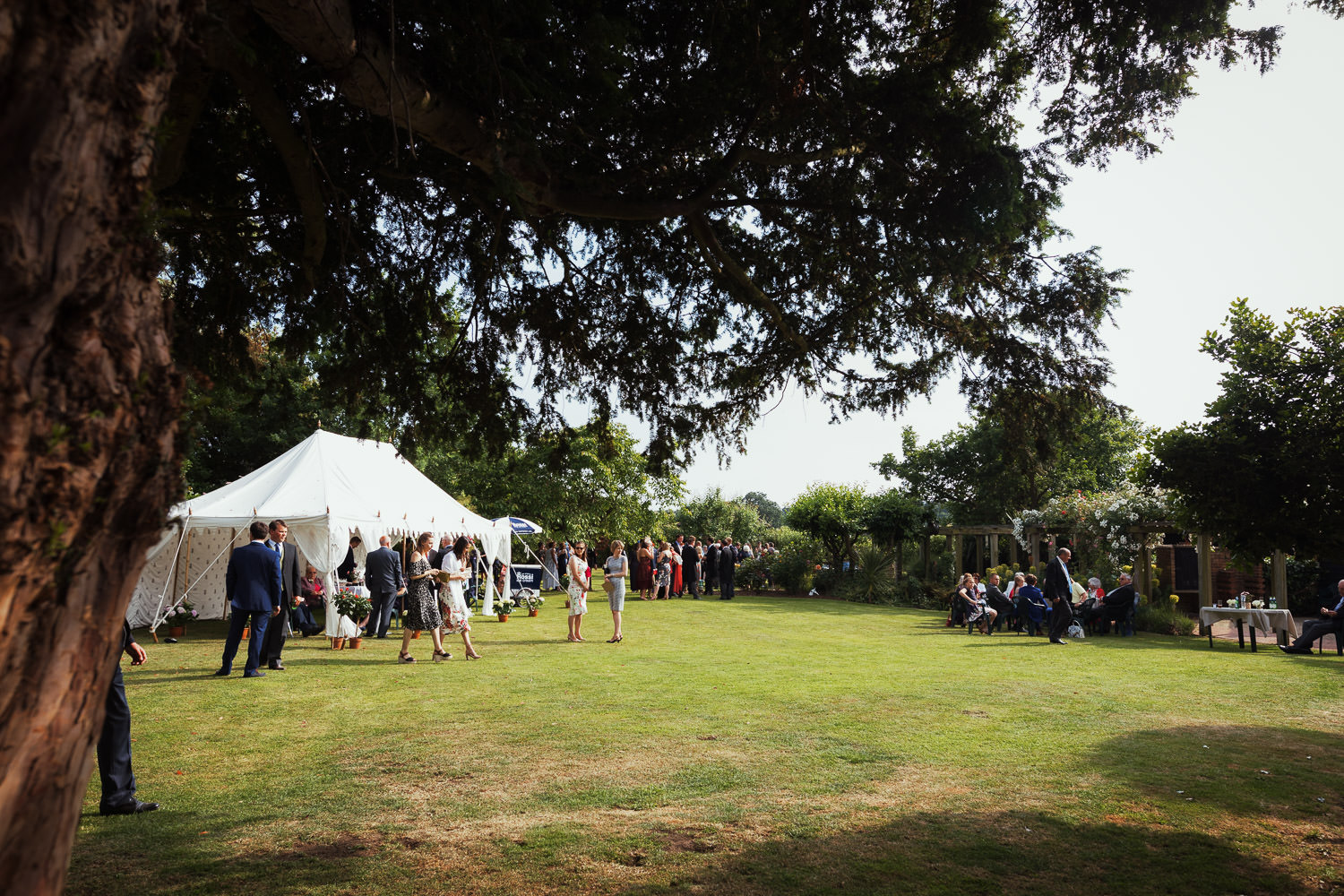 Wedding guests on the lawn. A tree and a small marquee, a wedding near Maldon in Essex.