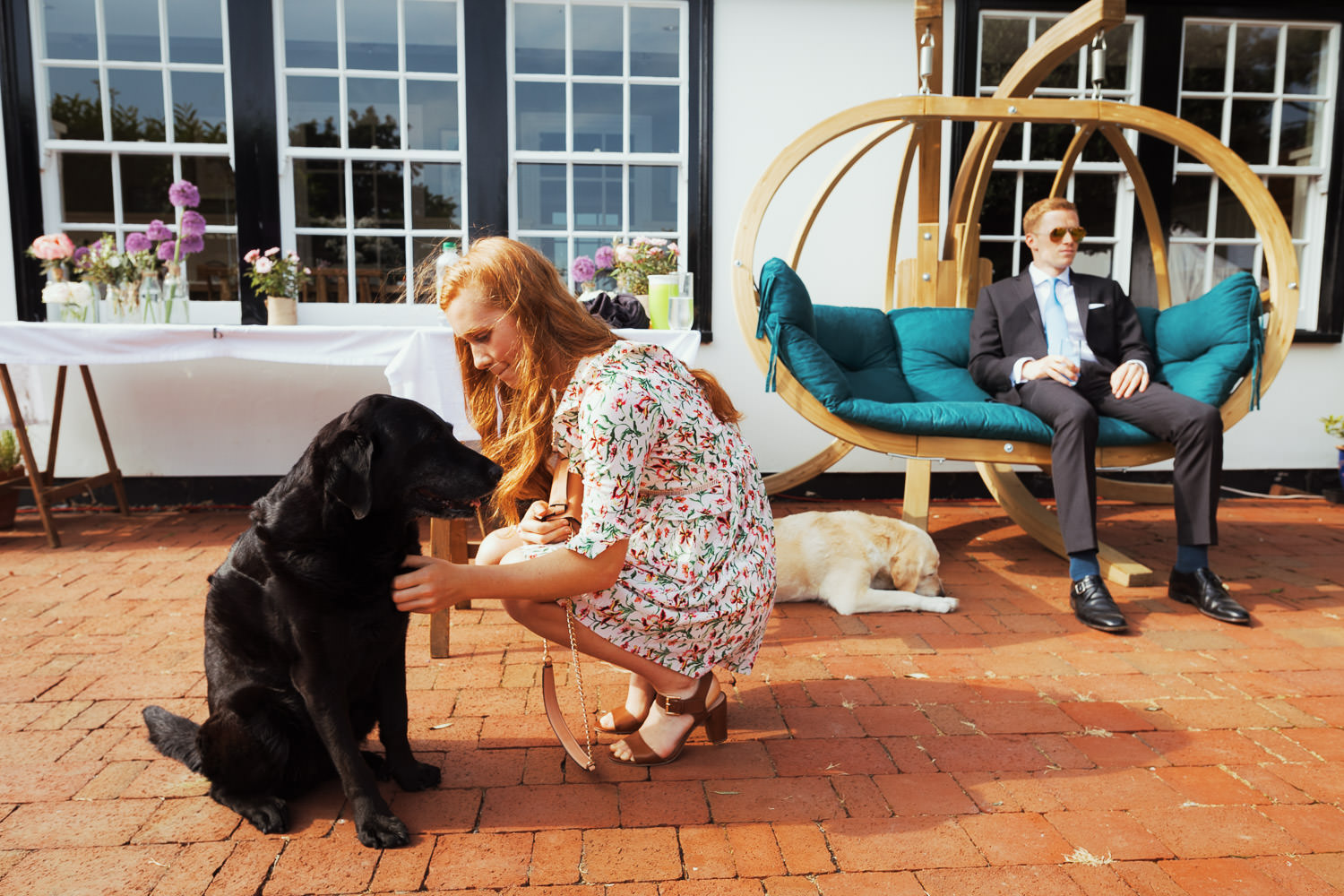 A woman in a floral dress petting a dog at a wedding.