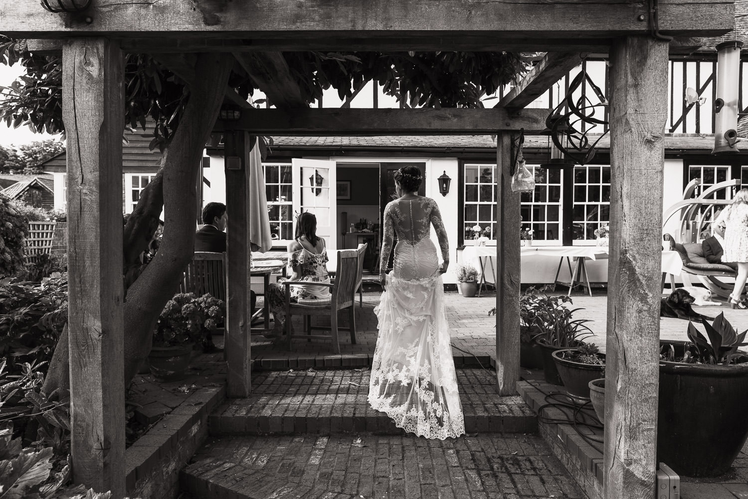 Woman in a wedding dress walking under a pergola towards the house.
