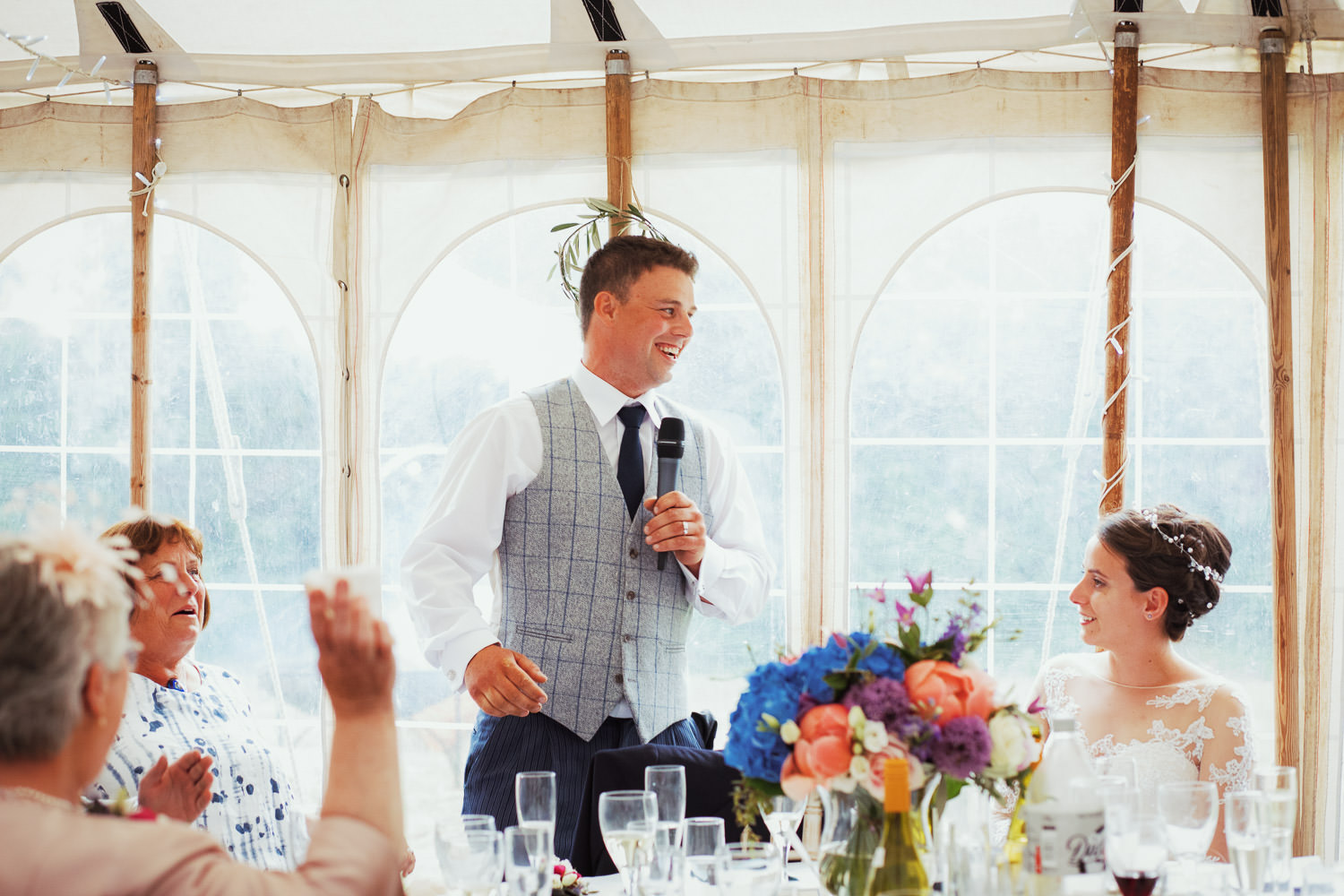 Groom giving a speech at a wedding breakfast in a white marquee.