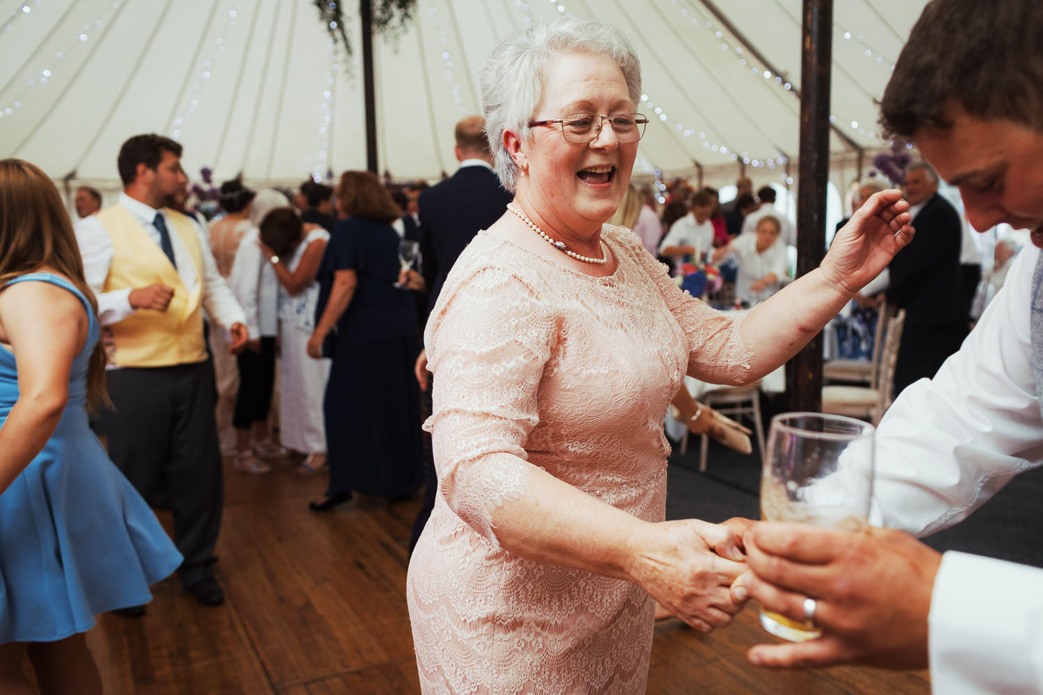 A woman in a peach dress dancing at a wedding in a marquee.