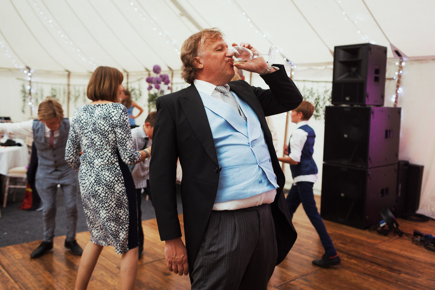 Man in a morning suit drinking wine on the dancefloor.