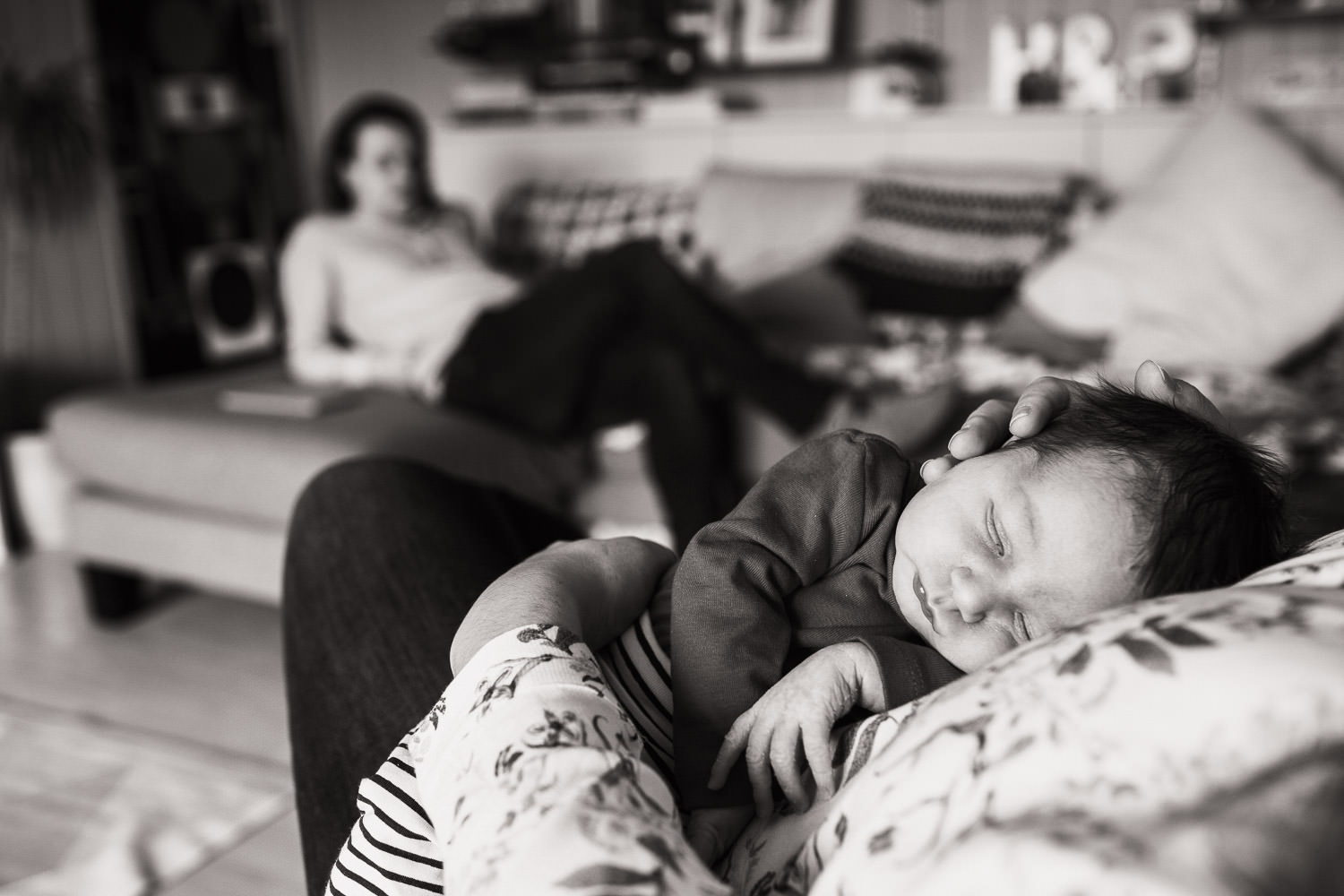 A newborn baby asleep on his mum, dad is in the background. Lifestyle family photography in Essex.