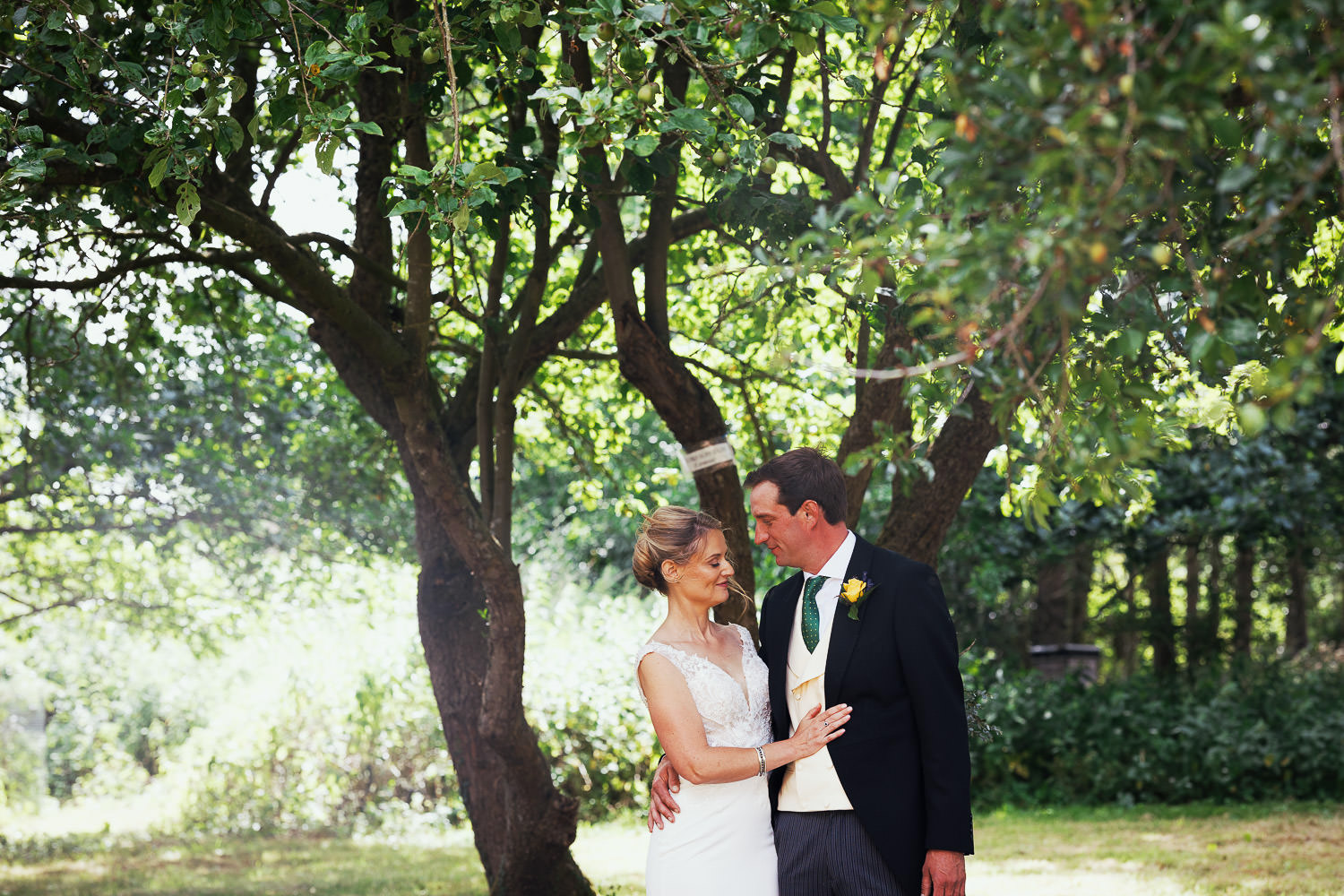 Bride and groom together under a tree in a Norfolk garden.