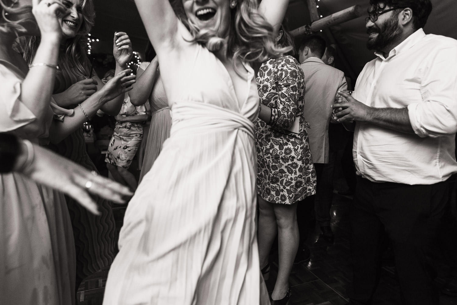 Bridesmaid jumps for joy while dancing at an evening reception in a tipi in a Suffolk garden, captured by a documentary wedding photographer from Essex.