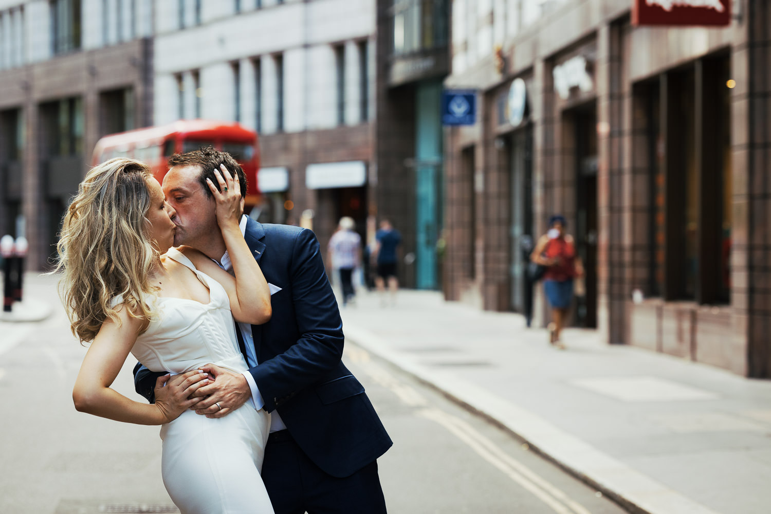 Bride is posing and kissing in road with her husband down St Mary Axe. There is a red bus behind them.