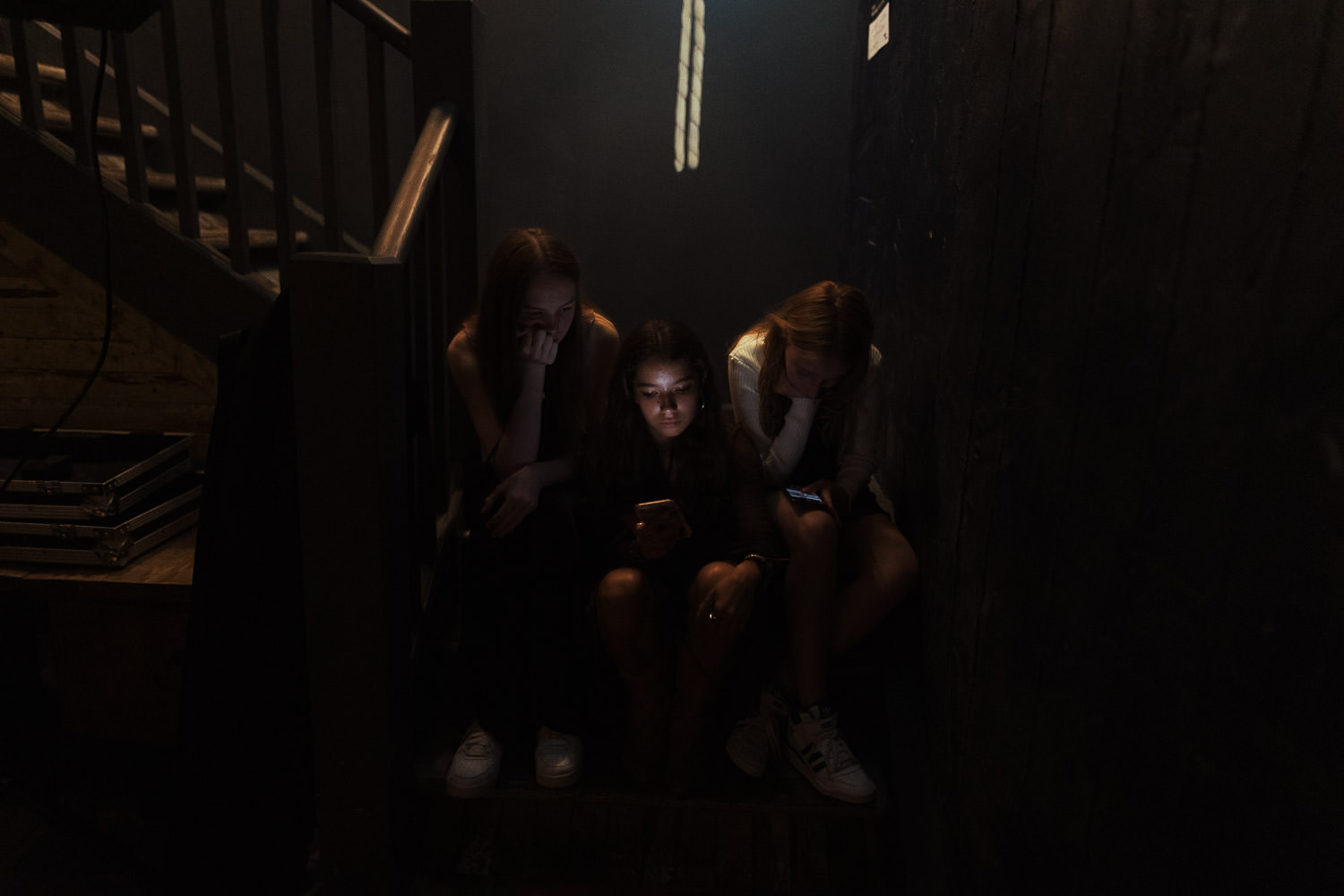 Three young women seated on the stairs at Never For Ever at wedding reception, absorbed in their smartphones. The image complements text emphasising that, owing to the photographer's reportage style, clients won't be disturbed on their wedding day for social media content videos.