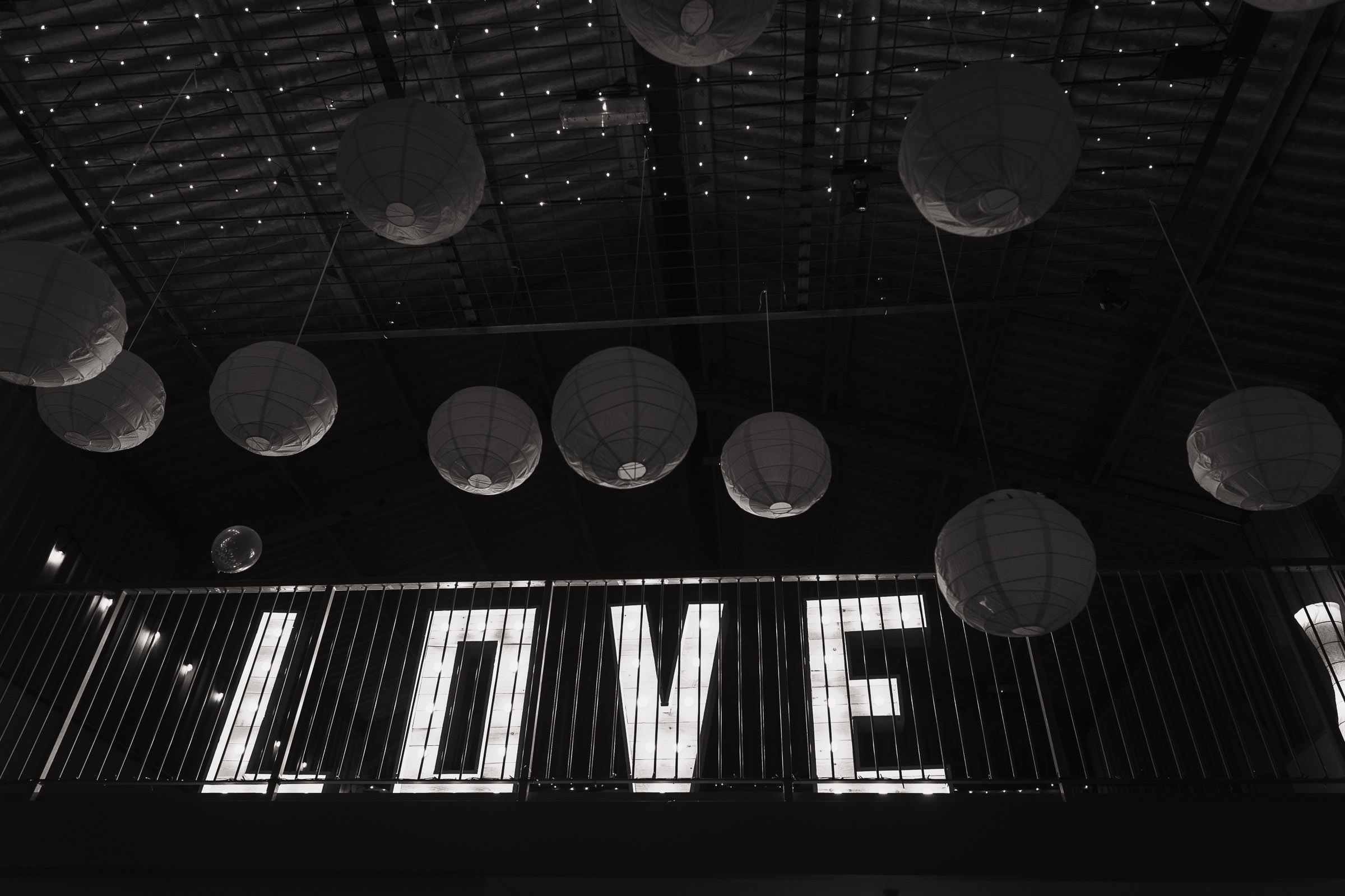 Giant letters spell the word LOVE at the wedding venue in Essex called Houchins. There are round paper lanterns on the ceiling.