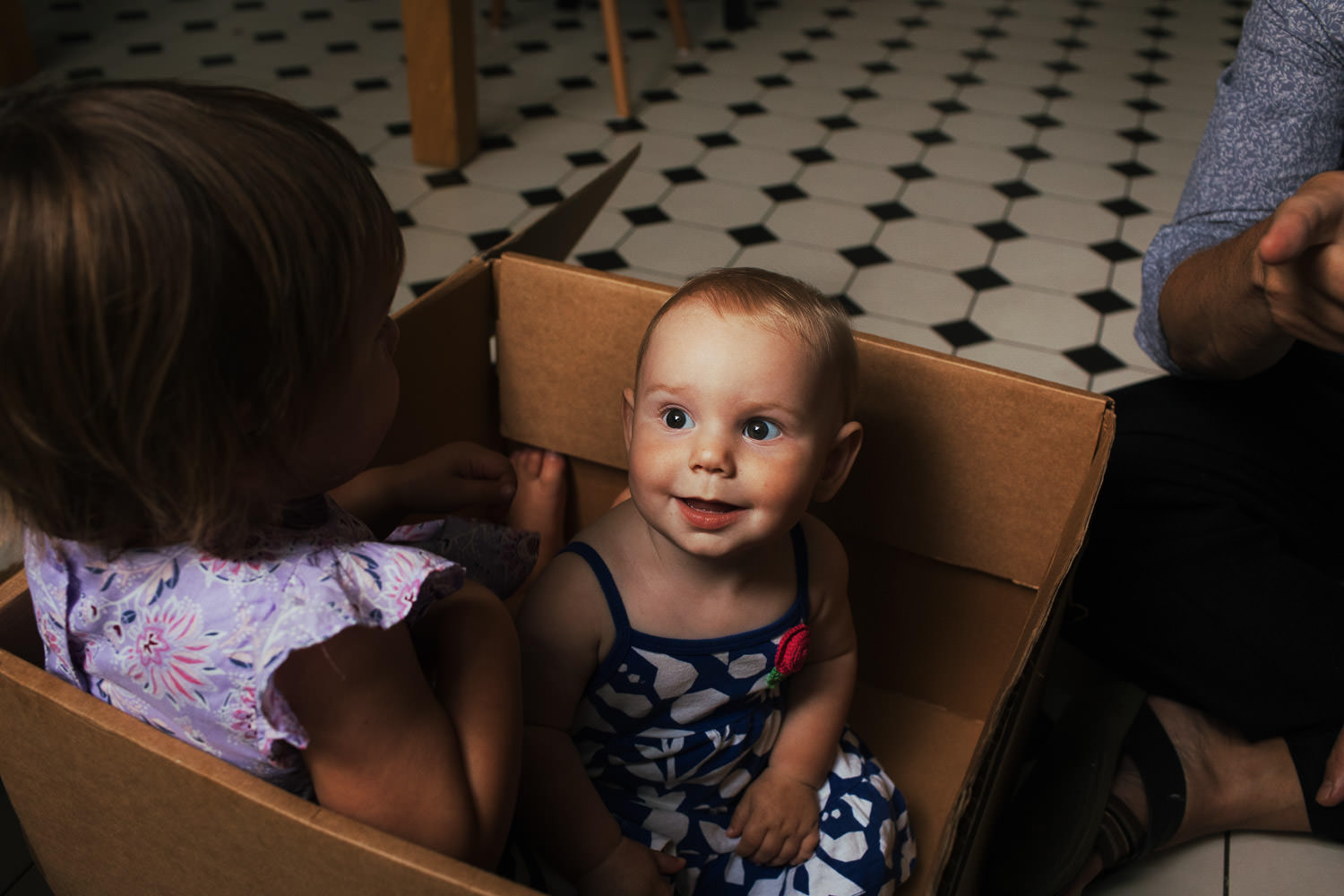 Baby and sister in a cardboard box. Documentary family photography in London.