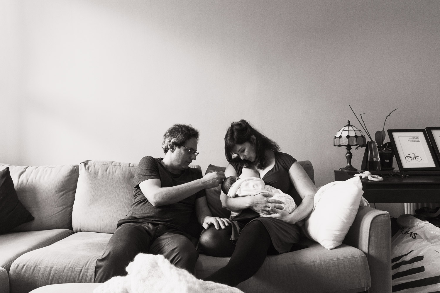 Mum feeding her baby, sat on the sofa with her husband. Relaxed family newborn photography at home.