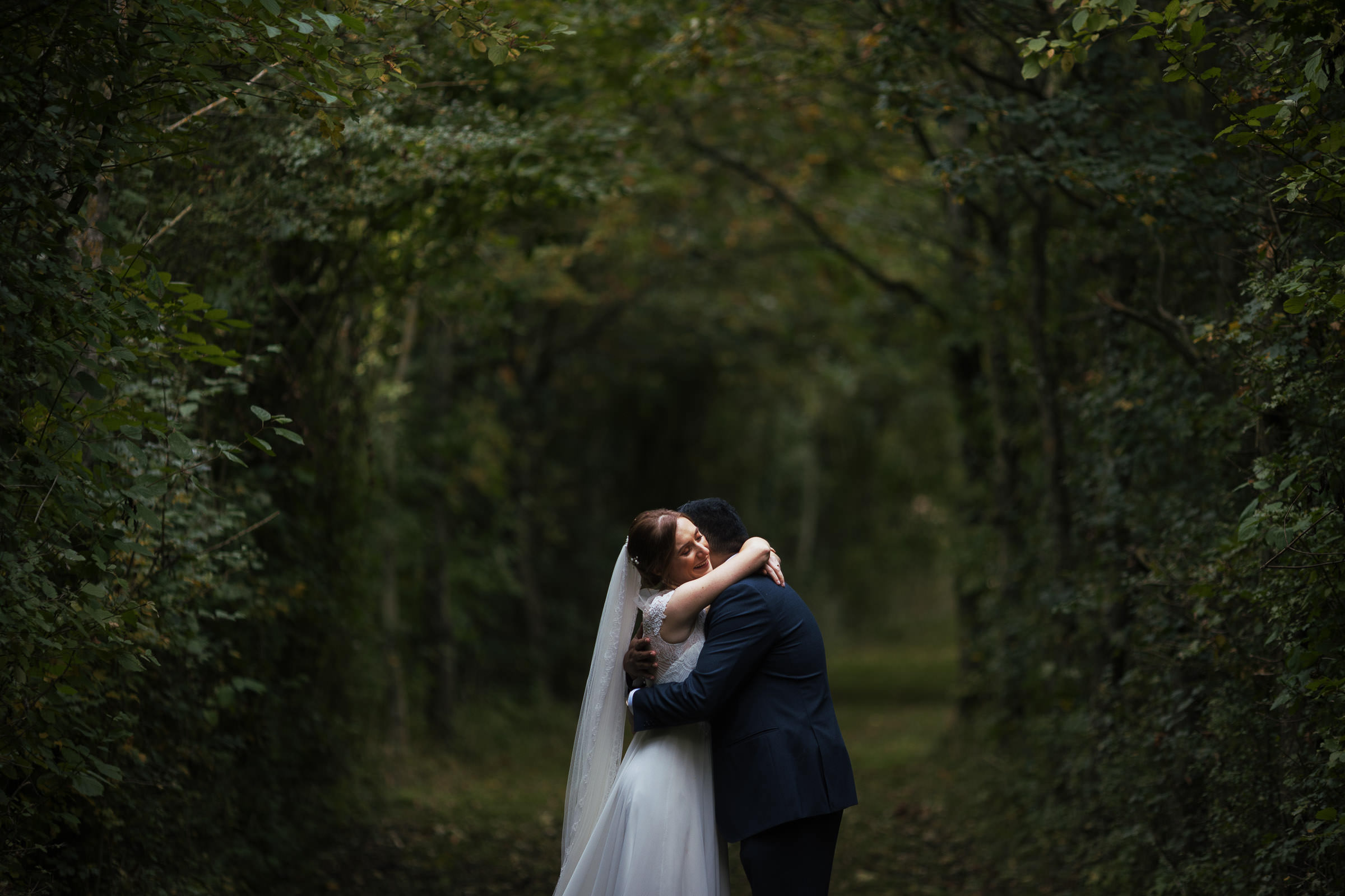 Newly married couple hug among the trees at Alpheton Hall Barns. An autumn wedding in Suffolk.