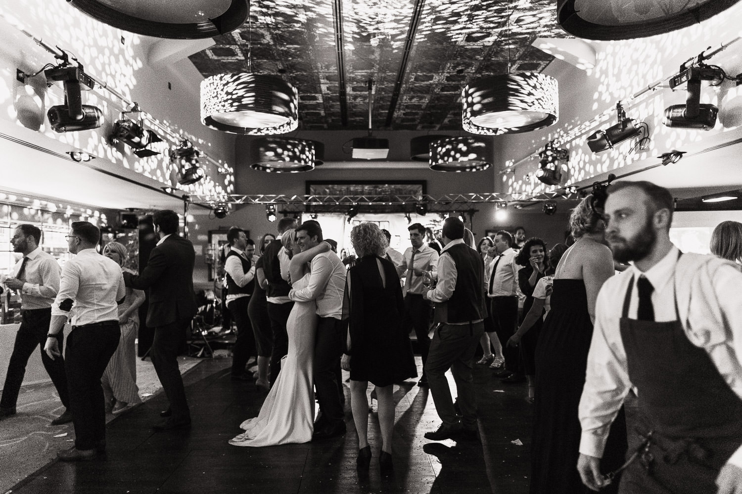 A documentary style wedding photography of a busy dance floor at The Lion House wedding venue in Essex. Bride and groom are dancing in the middle, a waiter walks past. Chelmsford wedding venue near the A12.