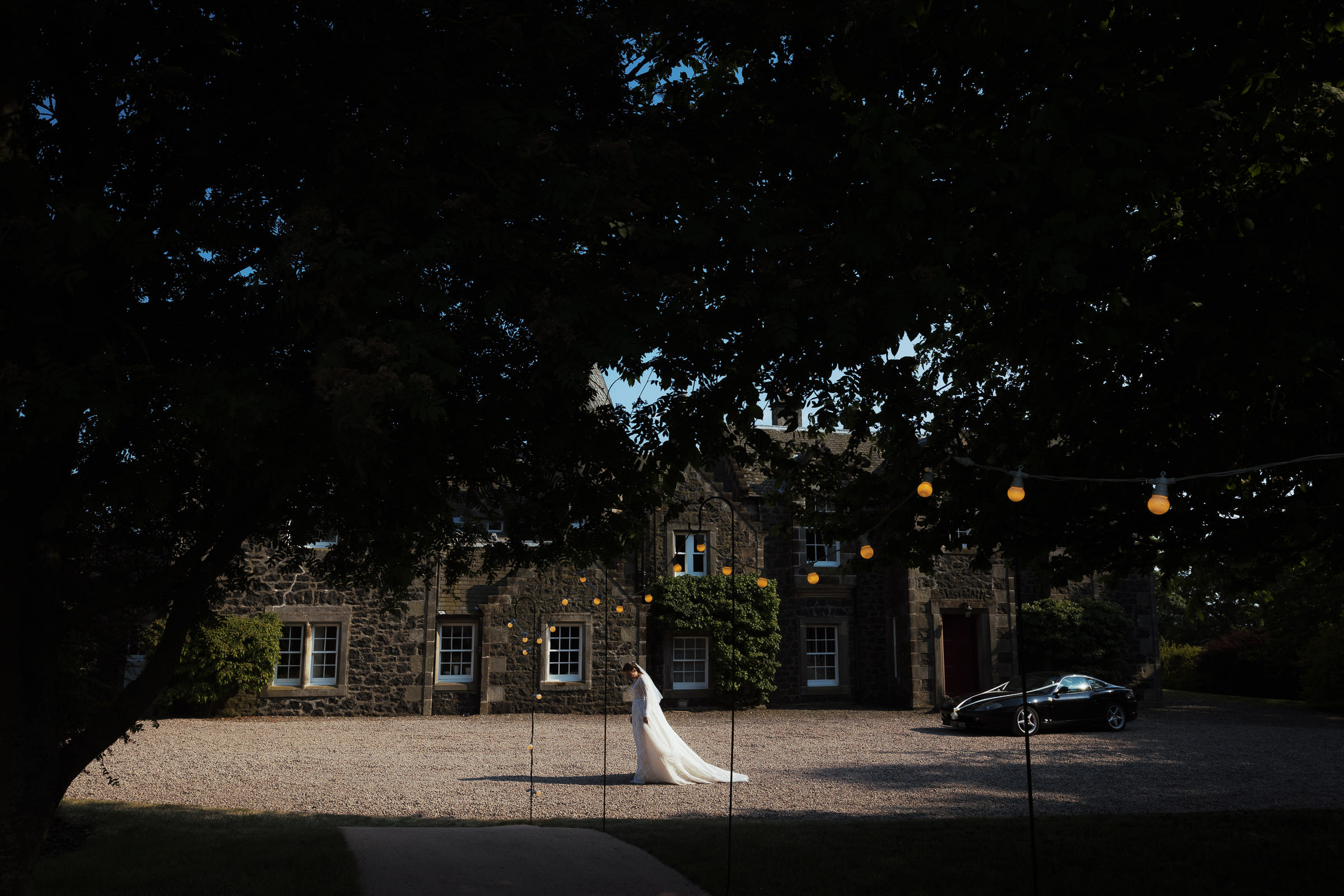 A wedding at a family home, marquee weddings. A bride stands on the driveway in the sunshine, she is wearing a dress called Minghas from Pronovias.