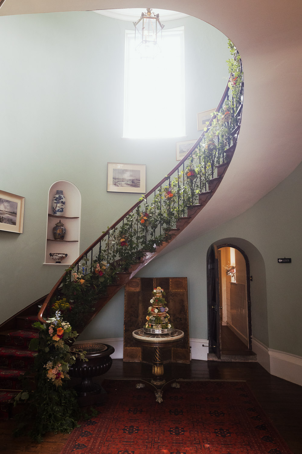 A flying staircase decorated with flowers from The Fabulous Florist. A cake on a round table. Made by The Couture Cake Company in Stourport-on-Severn.