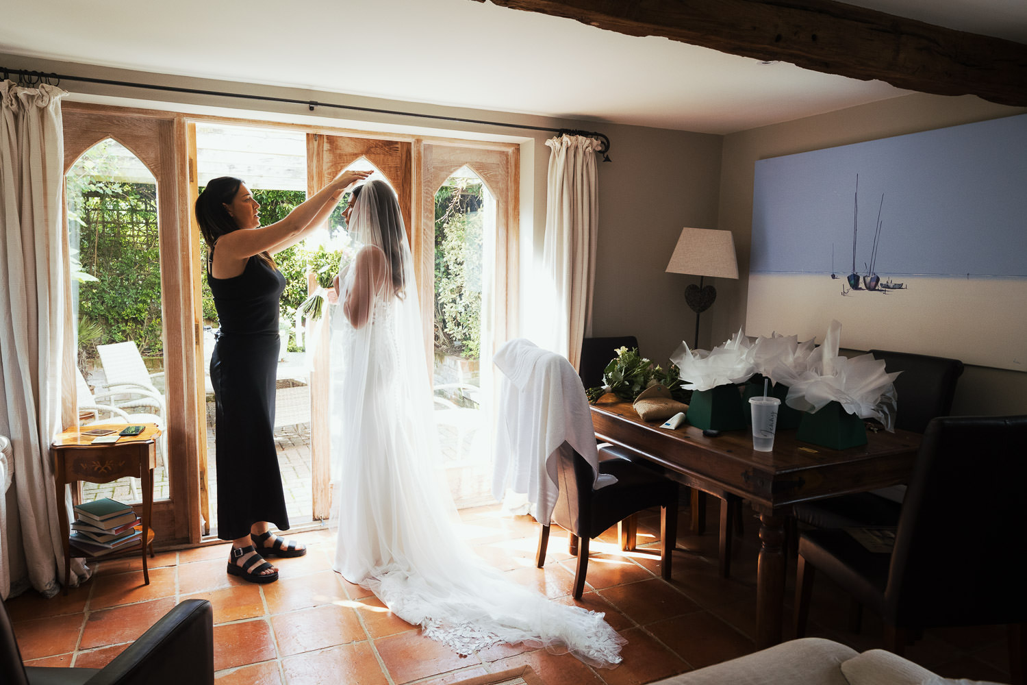 Hollie of Glow Occasion Hair, the finishing touches to the bride's hair and veil. Standing in the light of the French doors in the lounge of The Priory Dairy in Lavenham.