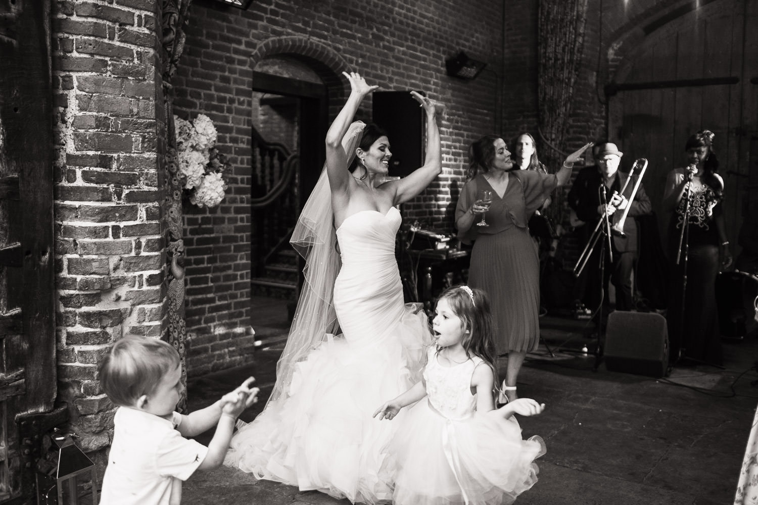 Woman in Pronovias Barcelona Mildred Wedding Gown is dancing with her hands in the air at reception. A wedding at Tudor manor house wedding venue in Essex called Leez Priory.