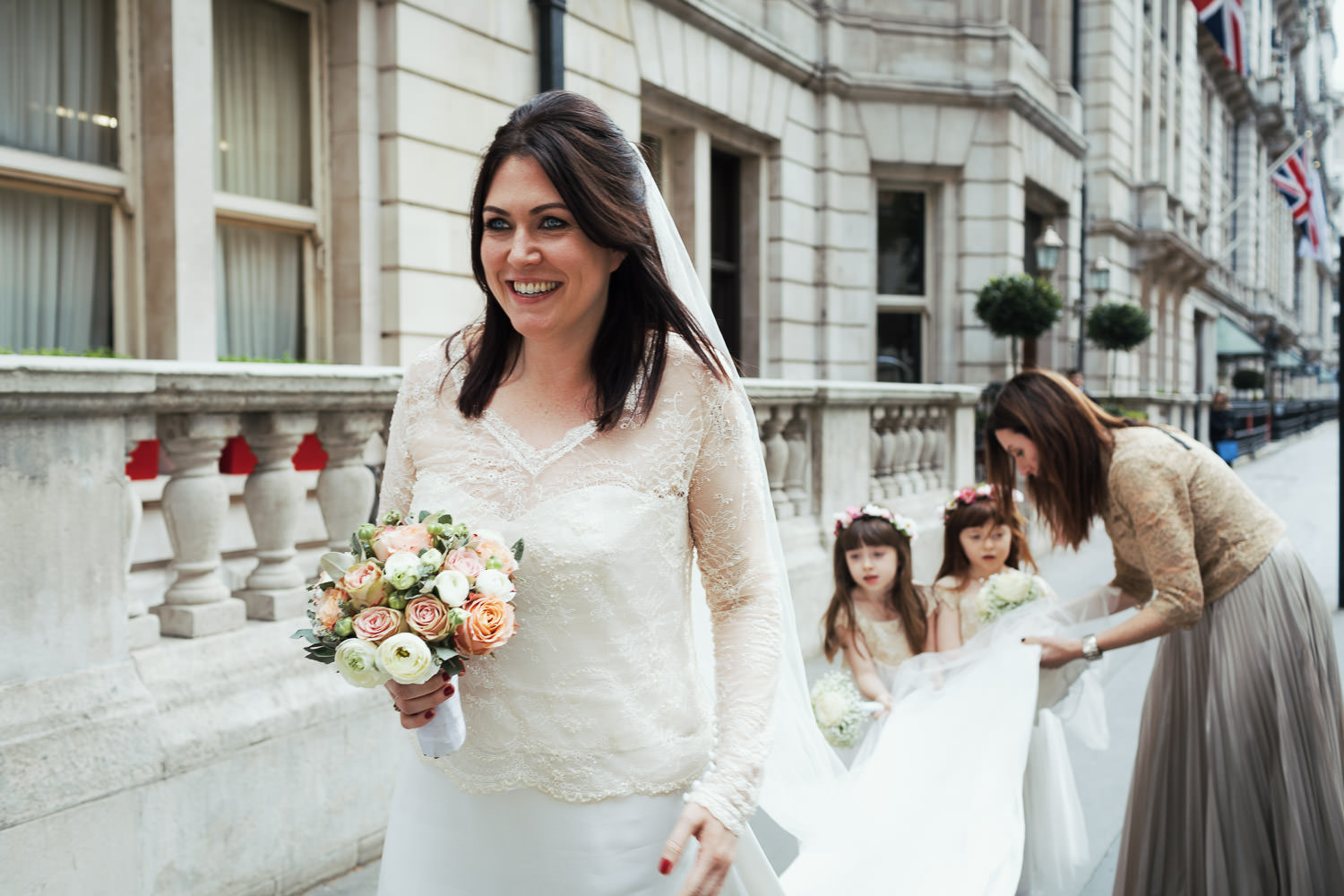 Bride arriving at The National Liberal Club at Whitehall Place, flower girls and sister holding her train and veil.