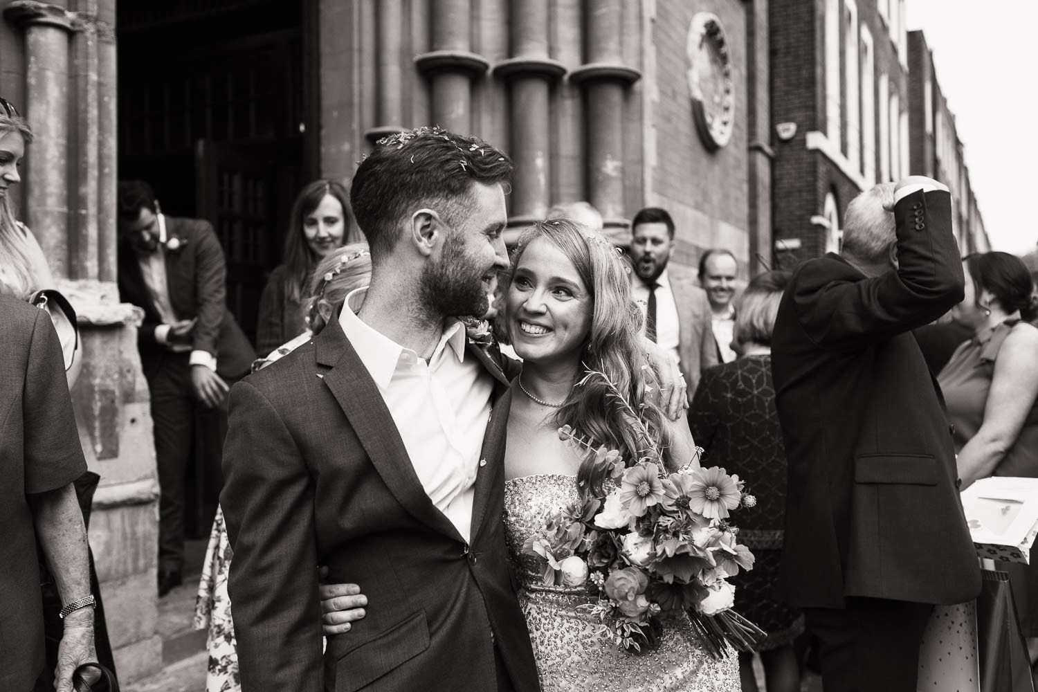 Newly married couple outside the steps of Union Chapel smiling at each other.