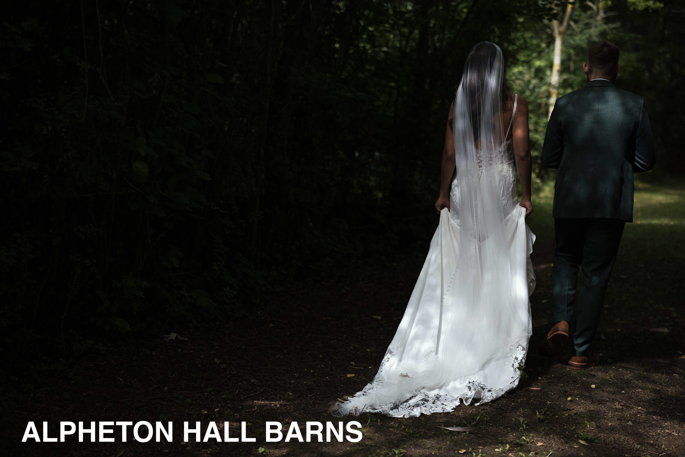 Alpheton Hall Barns Wedding Photography: Bride and groom walking down the tree lined lane.  Bride is wearing Maggie Sottero-Baxley 22MW548B01.