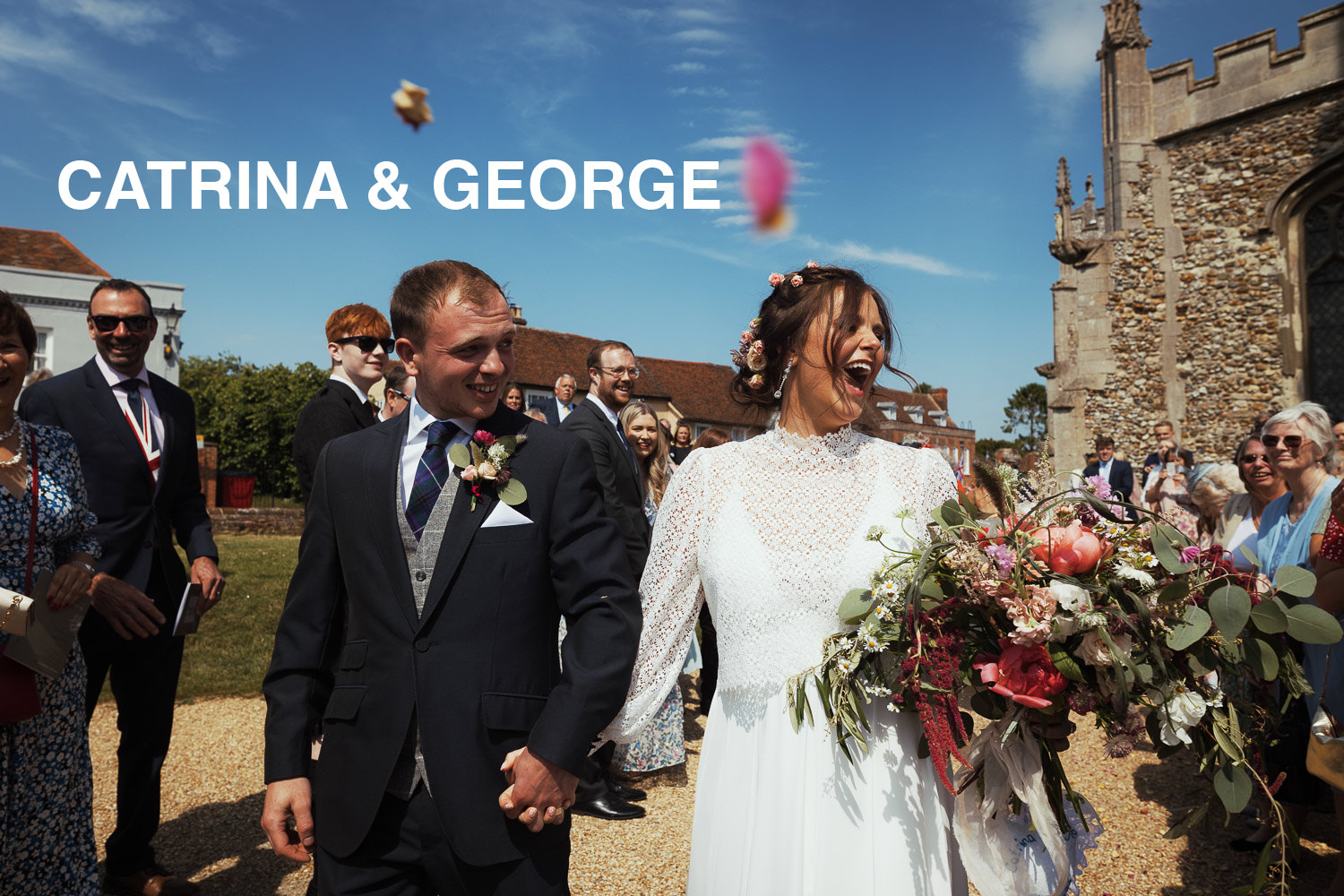 A bride and groom leaving the Thaxted Parish church after their wedding. Guests throw confetti, the sky is blue on a sunny day.