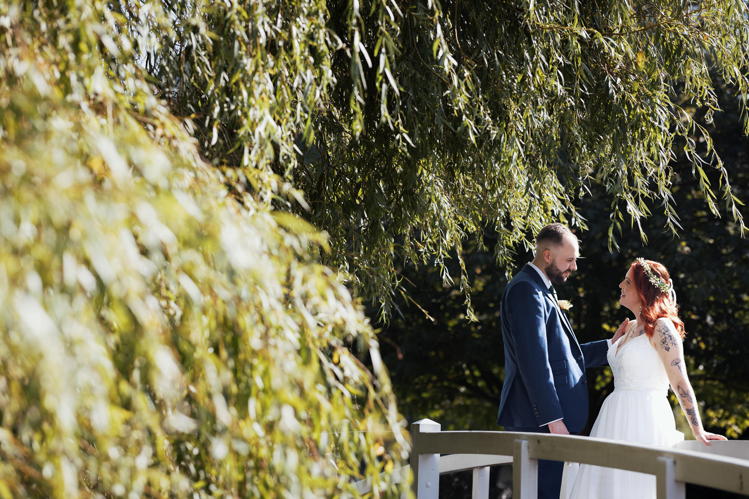 The newly married talking on the bridge under the weeping willow. High House Weddings, Old Heath Rd, Althorne, Chelmsford CM3 6EW